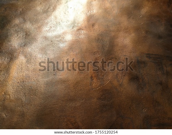 Copper texture background. Bronze texture. Bent\
metal with dents. Close-up of a bronze surface. A reflection of\
light in a bent place