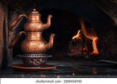 Copper Turkish Teapots On Metal Stand With Coals On The Edge Of The Stove. Making Tea In The Morning By The Chef Before Working In The Kitchen. Fire Is Burning In The Stove. Close-up