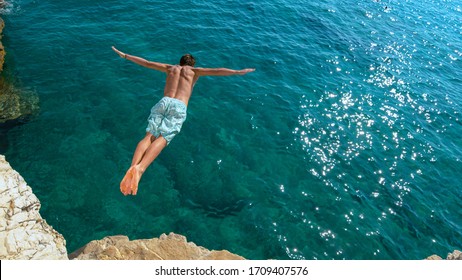 COPY SPACE: Athletic young man jumping off a rocky ledge and into the glistening blue ocean. Unrecognizable male tourist on a relaxing summer vacation in does cliff diving on a beautiful sunny day.