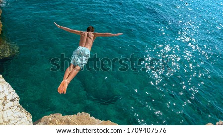 COPY SPACE: Athletic young man jumping off a rocky ledge and into the glistening blue ocean. Unrecognizable male tourist on a relaxing summer vacation in does cliff diving on a beautiful sunny day.
