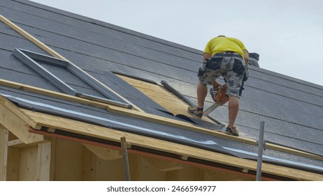 COPY SPACE Builder stands atop an unfinished roof and saws an opening in the wood before contractors mount a skylight. Worker uses a chainsaw to cut out a piece of the timber roofing for a roof window - Powered by Shutterstock