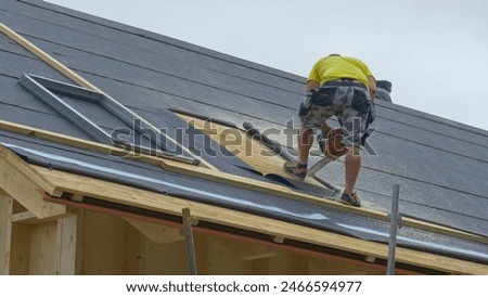 COPY SPACE Builder stands atop an unfinished roof and saws an opening in the wood before contractors mount a skylight. Worker uses a chainsaw to cut out a piece of the timber roofing for a roof window