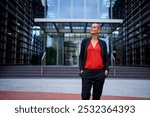 Copy space of empowered adult business woman in suit posing standing looking upwards with confident gesture in front of modern office building. Attractive female in leadership attitude outdoors