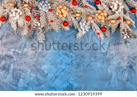 Copy space on a dark blue background with putty texture. Christmas composition, snow covered fir branches. They are decorated with golden bows, golden Christmas balls and red berries. Festive layout