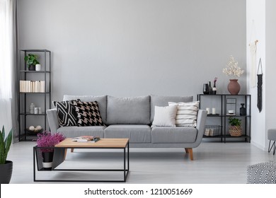 Copy space on the wall of scandinavian living room with modern couch, metal shelves and industrial coffee table, real photo