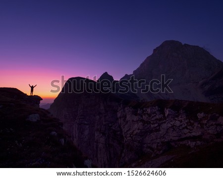 COPY SPACE, SILHOUETTE: Cinematic shot of a cheerful female hiker outstretching arms after reaching the summit just before sunrise. Joyful trekker celebrates reaching the mountaintop at golden sunset.