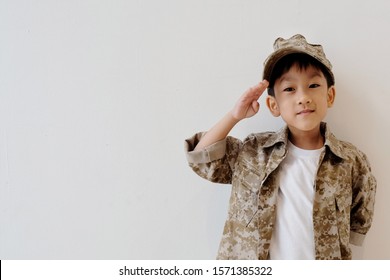 Copy Space And Soft Focus At Little Asian Kid 5 Year Old Smile And Wear Soldier Suit, Portrait Handsome Boy Wear Military Uniform And Stand At Salute. Clasped Behind Back. Concept Dream And Occupation