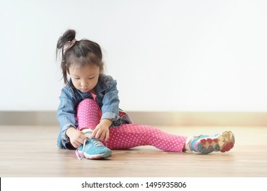 Copy Space And Soft Focus Portrait Cute Little Asian Girl 3 Year Old Sit On The Ground And Try To Tie Her Shoes. Beautiful Kid Try To Shoelace By Herself. Concept First Step , Growth Up And Moving On.