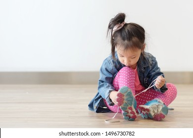 Copy Space And Soft Focus Portrait Cute Little Asian Girl 3 Year Old Sit On The Ground And Try To Tie Her Shoes. Beautiful Kid Try To Shoelace By Herself. Concept First Step , Growth Up And Moving On.