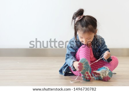 Copy space and Soft focus portrait cute little Asian girl 3 year old sit on the ground and try to tie her shoes. Beautiful kid try to shoelace by herself. concept first step , growth up and moving on.