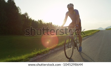 COPY SPACE, SUN FLARE: Pro road cyclist racing through the countryside in the afternoon. Active young man rides his bicycle through picturesque summer nature. Relaxing bicycle ride through the country