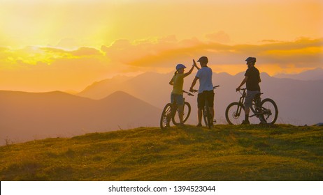 COPY SPACE Three Young Friends Celebrate A Successful Cross Country Bike Trip On A Sunny Summer Evening In Idyllic Slovenian Mountains. Tourists Ride Bicycles Up To Edge Of A Grassy Hill And High Five