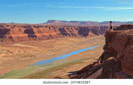 COPY SPACE: Young woman exploring the American wilderness sits on the edge of a cliff overlooking the disappearing Lake Powell. Traveler observes famous Lake Powell drying up due to climate change. - Powered by Shutterstock