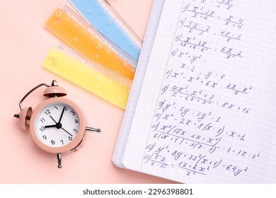 Copybook with maths formulas, alarm clock and rulers on pink background