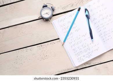 Copybook with maths formulas, alarm clock, pen and pencil on beige wooden background