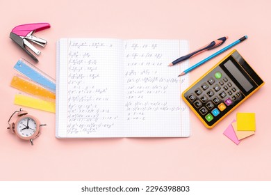 Copybook with maths formulas, calculator, alarm clock and stationery on pink background