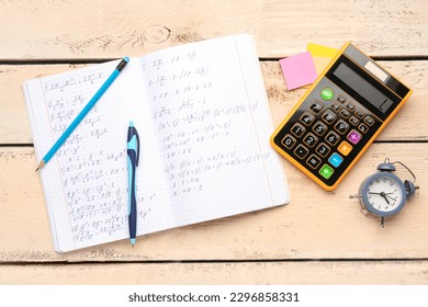 Copybook with maths formulas, calculator, alarm clock and stationery on beige wooden background