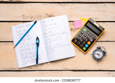 Copybook with maths formulas, calculator, alarm clock and stationery on beige wooden background