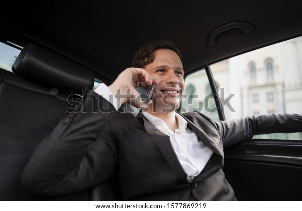 Copyspace: Businessman is making a call with smiling\
expression while riding a\
car