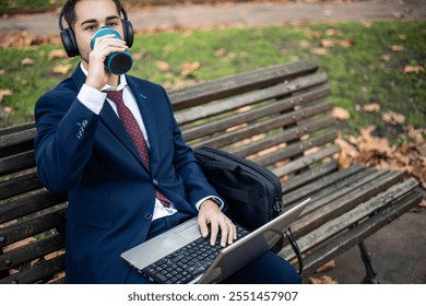 copyspace busy businessman takes a coffee break while continuing to work on his laptop, seated on a park bench. Despite the break, he remains focused on his tasks, blending relaxation and productivity - Powered by Shutterstock