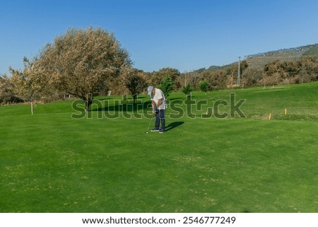 copyspace elderly golfer standing on the green, concentrating deeply as he prepares to hit the ball with his putter. The image captures the calm and focus required for a successful putt