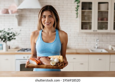 Copy-space Photo Of Attractive Young Lady Standing In Kitchen With An Array Of Protein-rich Food On Wooden Board In Hands