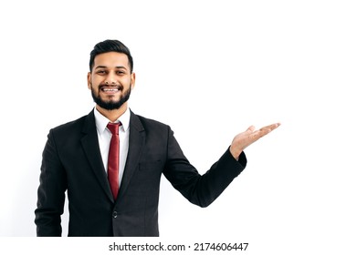 Copy-space For Your Presentation. Positive Elegant Arabian Or Indian Man In Formal Suit, Standing Over Isolated White Background, Looking At Camera, Pointing Hand To Empty Space, Smiles Happily