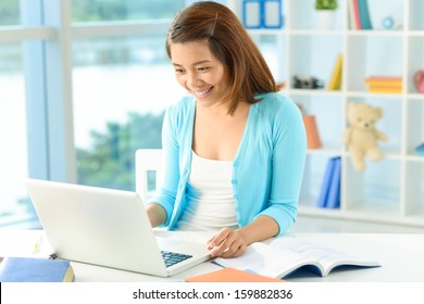 Copy-spaced image of a young lady networking at home while doing her homework on the foreground