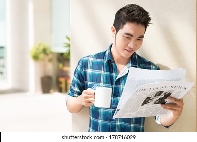 Copy-spaced Image Of A Young Man Reading The Local News With A Cup Of Tea On The Foreground 