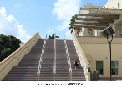 Coral Gables FL/USA: Nov 30, 2017 – Lone Woman Sits With Chin On Hand On High Outdoor Staircase At Watsco Center Which Is Home To The University Of Miami Hurricanes Basketball Teams. 