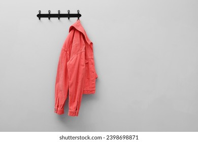 Coral jacket hanging on coat rack on light grey wall, space for text