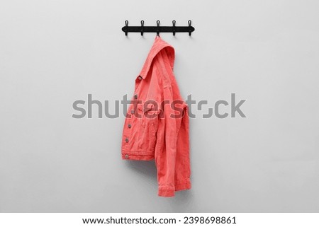 Coral jacket hanging on coat rack on light grey wall