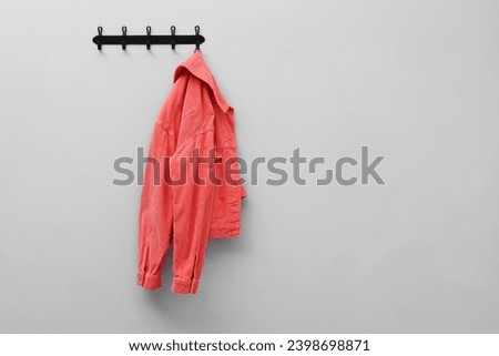 Coral jacket hanging on coat rack on light grey wall, space for text