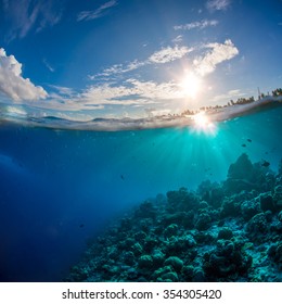 Coral reef in tropical ocean under water surface. Sunbeams light running through aquatic ripples. Beautiful design postcard on blue marine background.