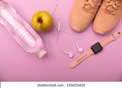 Coral Sport Shoes, Smart Watch, Earphones, Green Apple And Bottle Of Water On A Purpule Background. Top View. Flat Lay. Concept Healthy Lifestyle, Sport And Diet.