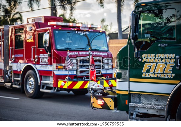 Coral Springs, Florida, USA - April 05, 2021:\
One red and one dark green fire truck with American and fire\
department flags parked next to each\
other.