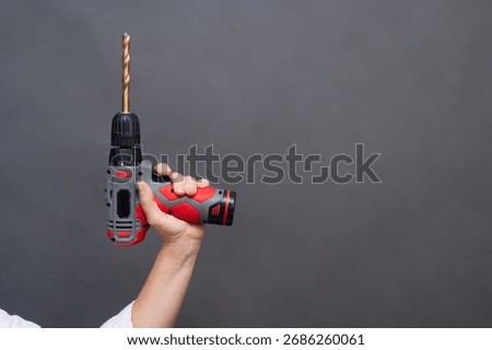 Cordless drill with long bit held in hand raised, power tool raised isolated neutral background, professional equipment. Hand holding cordless drill with extended drill bit, modern power tool isolated