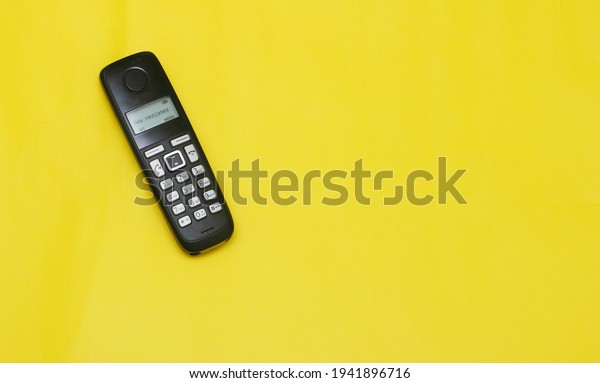 A cordless phone with dial pad placed on a yellow\
background 