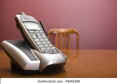 A Cordless Phone On A Table With An Out Of Focus Chair