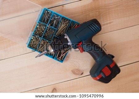 cordless screwdriver on the background of wooden boards. organizer box with hardware-screws, bolts, screws, nails,