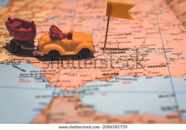 Cordoba, Spain pinned on map of Europe with yellow flag\
with car and boat next to it illustrating road trip to camping area\
or other vacation travel adventures with friends and family for\
holidays. 
