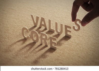 CORE VALUE wood word on compressed or corkboard with human's finger at S letter.
