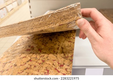 Cork floor in sheets. Purchase of cork flooring, thin sheets for laying. A man takes a pack of cork sheets from a shelf in a store