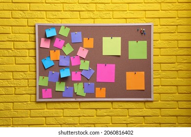Corkboard filled with colorful notes and pins on yellow brick wall