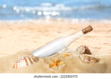 Corked glass bottle with rolled paper note and seashells on sandy beach near ocean