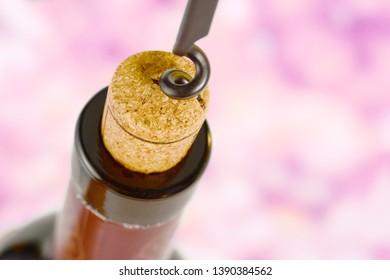 Corkscrew pulls out a cork from the bottle of red wine. Cork close-up macro. on pink background.