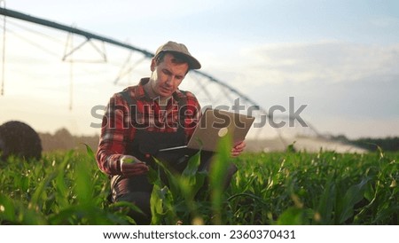 corn agriculture. male farmer works on a laptop in a field with green corn sprouts lifestyle. corn is watered by irrigation machine. irrigation agriculture business concept