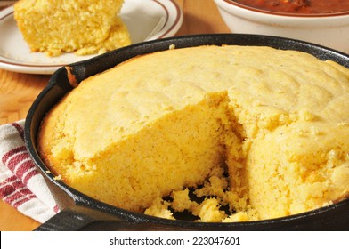 Corn Bread In A Cast Iron Skillet With A Bowl Of Chili In The Background