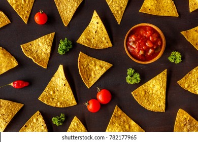 Corn Chips Nachos And Chunky Tomato Salsa In A Wooden Bowl, Cherry Tomatoes, Chilly Pepper And Parsley On A Dark Brown Wooden Surface. Square Image. Top View. 