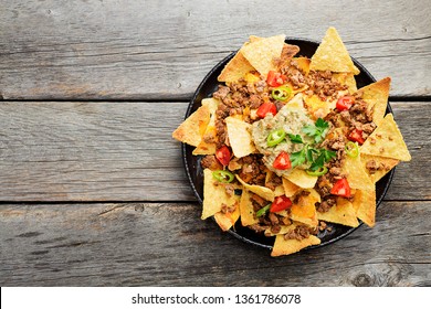 Corn chips nachos with fried minced meat and guacamole on wooden background.